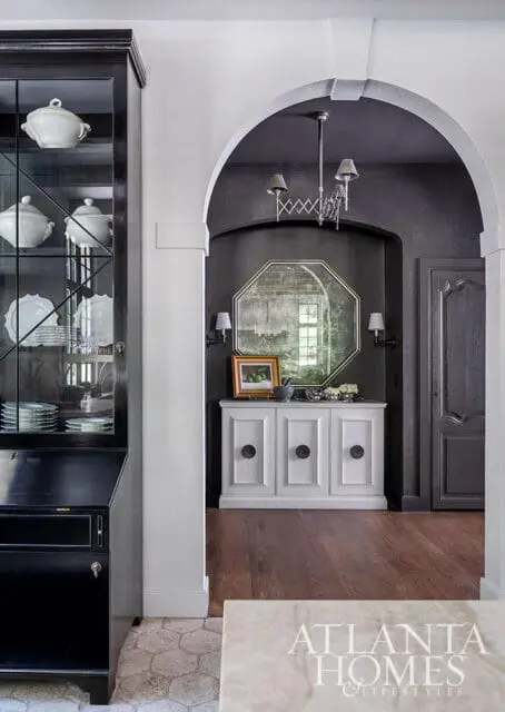 Black china cabinet with white dishes, arched doorway with octagonal mirror and white buffet