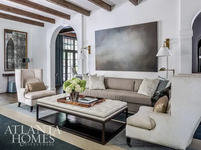 Living room with tufted ottoman coffee table, neutral sofa, and wingback chairs.