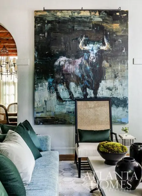 Abstract painting of a bull above a cane-backed chair and light blue sofa