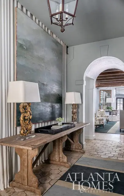 Hallway with large abstract painting, ornate gold lamps on wooden console table, and arched doorway