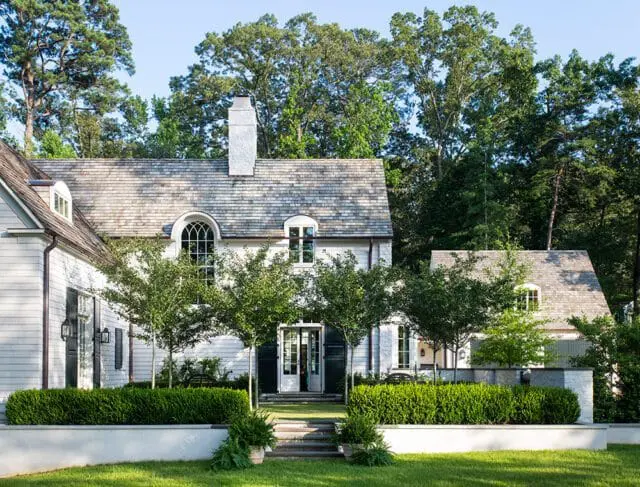 White house with gray shingle roof, arched windows, and manicured hedges