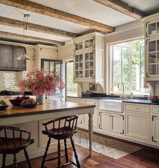Cream kitchen with exposed wood beams, farmhouse sink, and island with wooden stools.