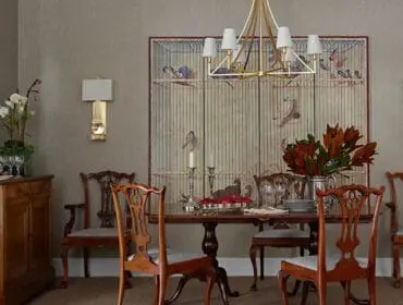 Dining room with antique chairs, a large birdcage painting, and a gold chandelier.