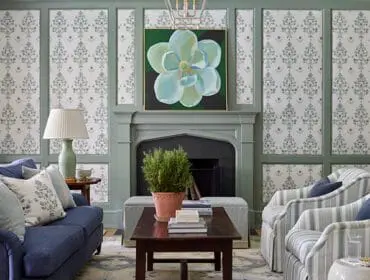 Living room with blue sofa, striped armchairs, floral wallpaper, and fireplace with magnolia