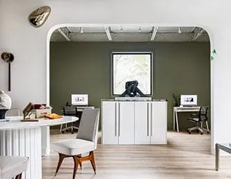 Modern office space with olive green walls, white cabinets, and two workstations.