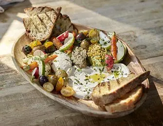 Wooden platter with whipped cheese, olives, cherry tomatoes, radishes, and grilled bread