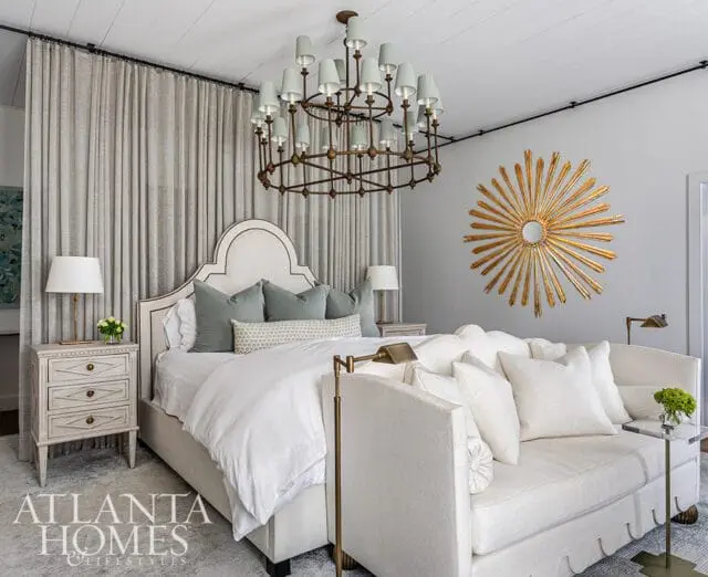 Bedroom with tufted headboard, sage green pillows, white bedding, and a sunburst mirror.