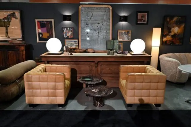 Tan leather tufted armchairs flank a wooden console with a large mirror and artwork.