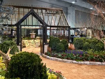 Greenhouse with dark metal frame, glass panels, and ornate roof details. Surrounded by manicured