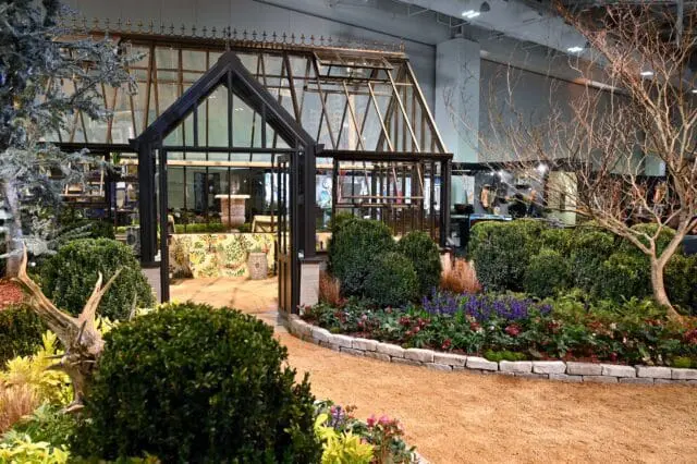 Greenhouse with dark metal frame, glass panels, and ornate roof details. Surrounded by manicured