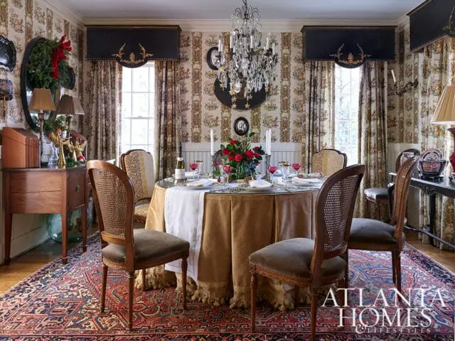 Dining room with round table set for a meal, crystal chandelier, floral wallpaper, and patterned