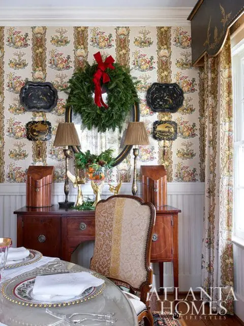 Dining room with festive wallpaper, a Christmas wreath, and a table set for a meal.