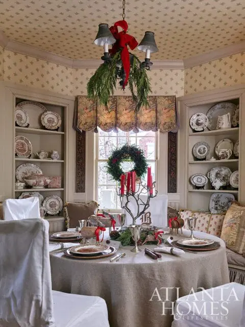 Dining room with a round table set for Christmas, featuring a wreath, candles, and festive decor.