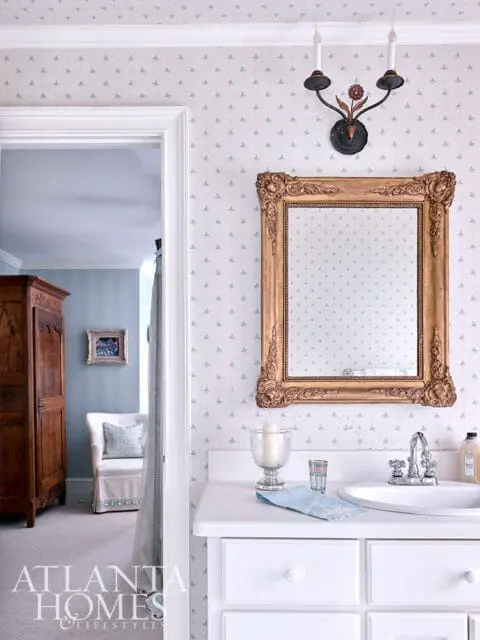 Bathroom with white vanity, ornate gold mirror, and patterned wallpaper.