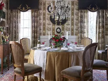 Dining room with floral wallpaper, round table set for dinner, crystal chandelier, and cane-back