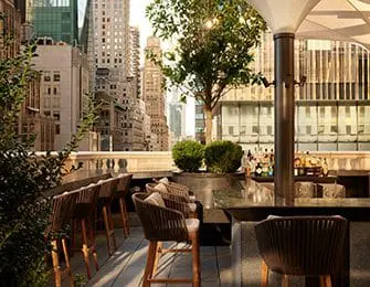 Rooftop bar with city skyline view, seating, and bar area.