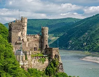 Castle on a cliff overlooking a wide river with green hills in the background