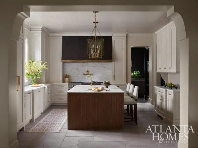 Cream kitchen with marble backsplash, dark range hood, and wood island with bar stools