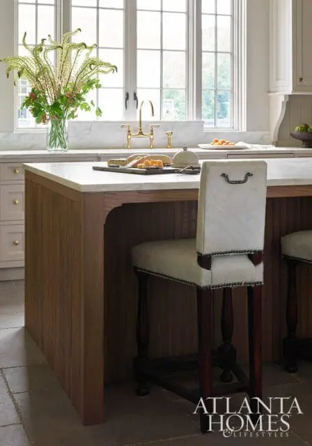 Kitchen island with marble countertop, wood base, and white upholstered bar stool.