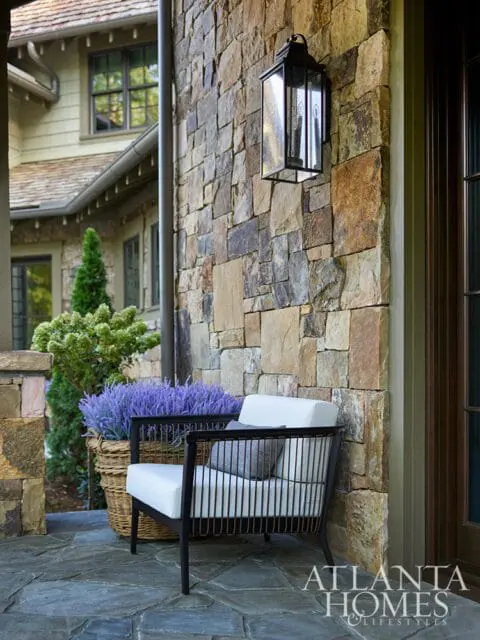Outdoor seating area with dark metal chair, lavender plants, and stone wall with lantern.