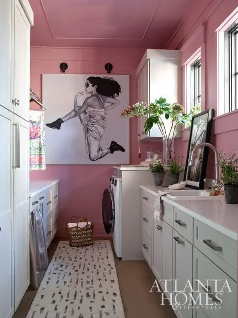 Pink laundry room with white cabinets, a large artwork of a jumping woman, and a patterned rug.