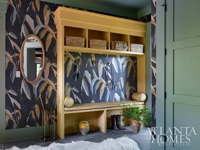Mudroom with yellow built-in bench and shelves, dark floral wallpaper, and green door.