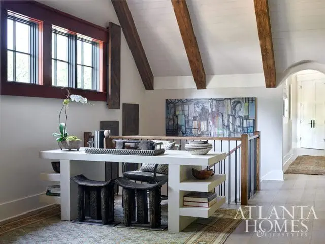 White desk with two carved stools, orchid, and abstract art above railing.