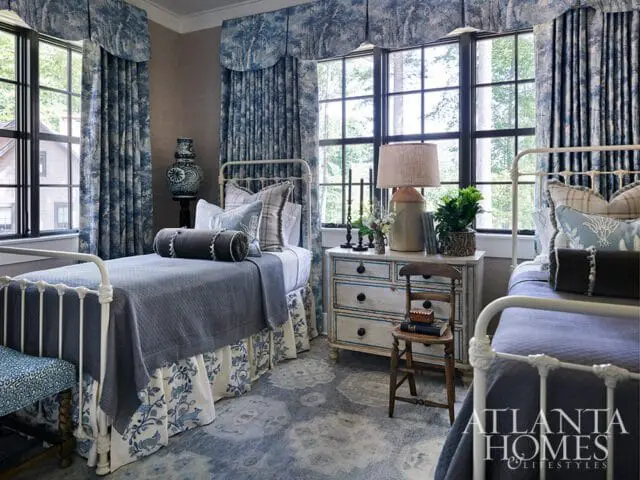 Bedroom with twin beds, blue toile curtains, and a distressed dresser.