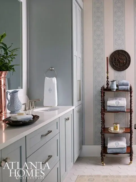 Light blue vanity with white countertop, silver faucet, and white towels. Striped wallpaper with