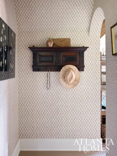 Hallway with patterned wallpaper, dark wood shelf with hat and vase, and Atlanta Homes & Lifestyles