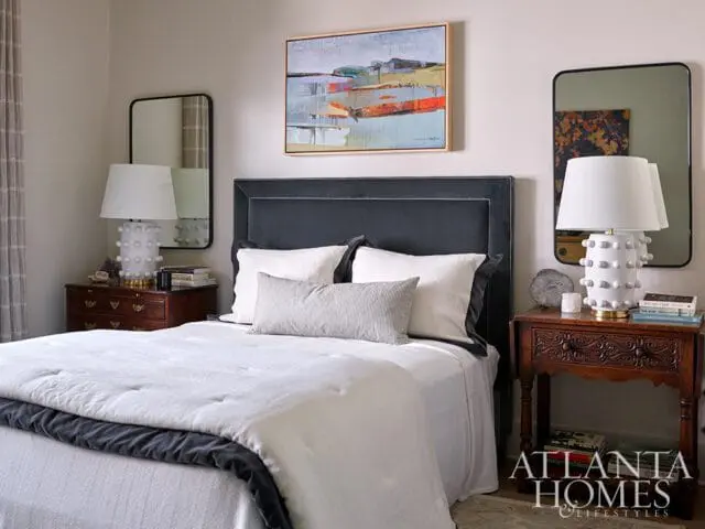 Bedroom with dark gray upholstered headboard, white bedding, and abstract art above the bed.