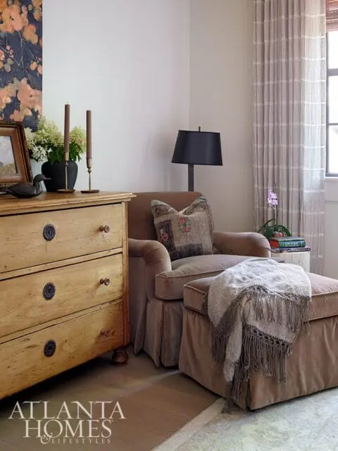 Brown armchair and ottoman with a fringed throw, next to a wooden dresser with decorative hardware.