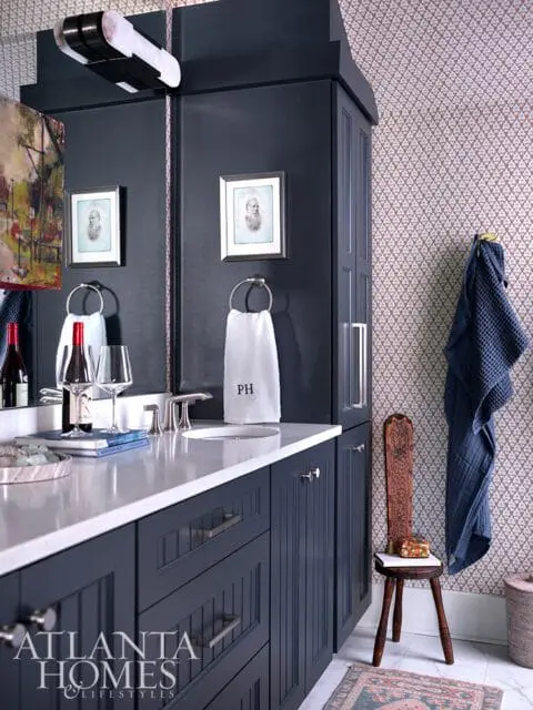 Dark blue vanity with white countertop, sink, and brass hardware. Patterned wallpaper.