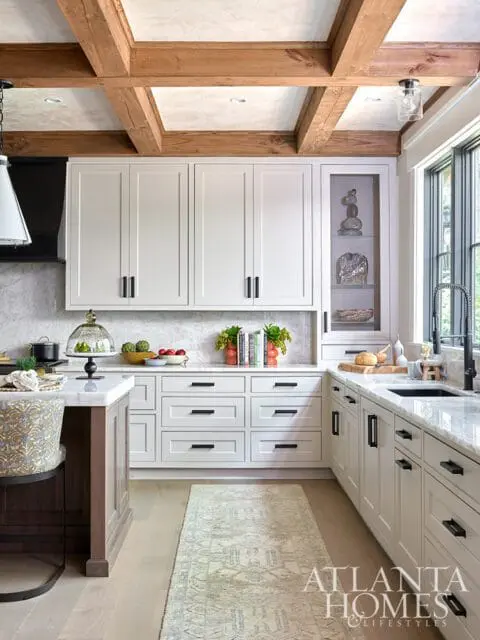 White kitchen with marble countertops, wood beam ceiling, and patterned rug