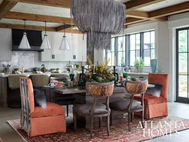 Dining area with rustic wood table, orange chairs, deer hide chairs, and large gray chandelier.