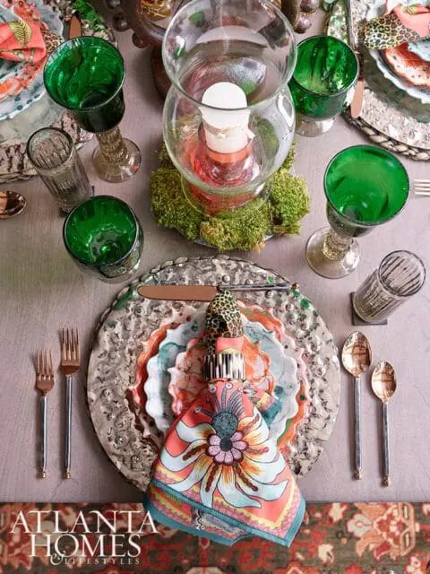 Table setting with green goblets, patterned napkins, and floral plates.