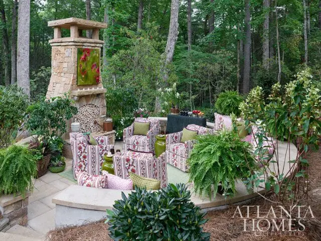 Stone fireplace with floral upholstered seating and lush greenery in a wooded setting.