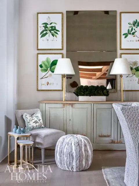 Living room with botanical prints, gray chair, distressed cabinet, and fur ottoman.