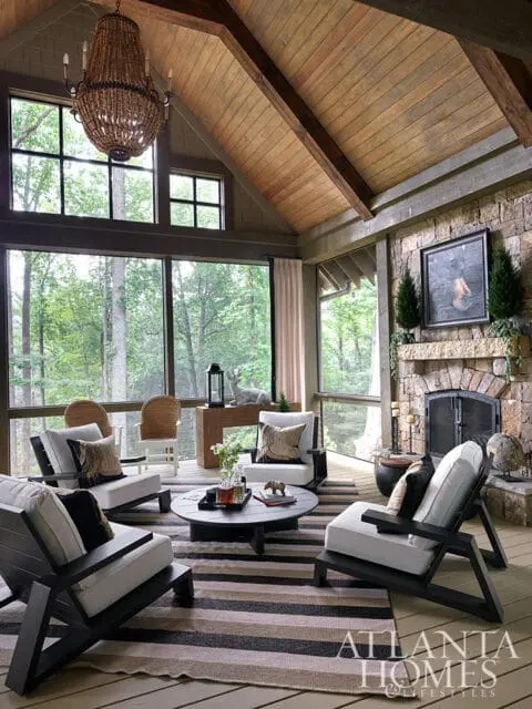 Screened porch with stone fireplace, wood ceiling, and seating area with striped rug.