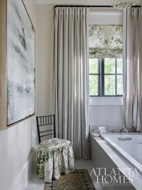 Bathroom with striped curtains, floral Roman shade, and a chair with a floral skirt.