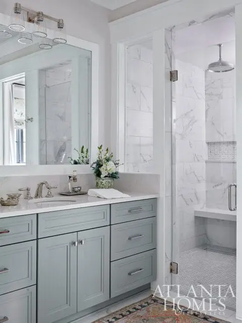 Bathroom with light blue vanity, marble shower, and glass door.