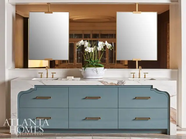 Blue vanity with marble countertop, brass hardware, and two hanging mirrors.