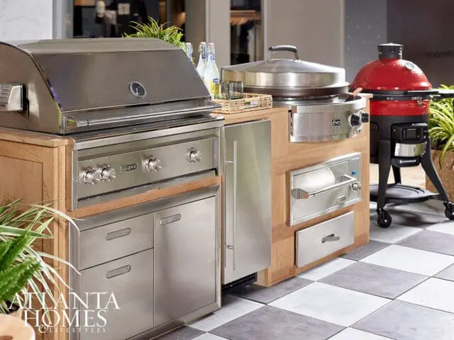 Outdoor kitchen with stainless steel grill, wood cabinetry, and red ceramic cooker.