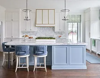 White kitchen with blue island, marble countertops, and brass pendant lights.