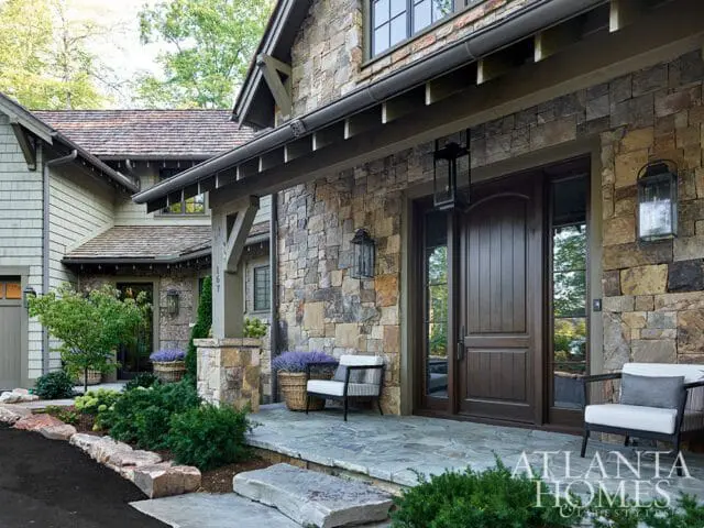 Stone house with wood double doors, porch seating, and landscaping.