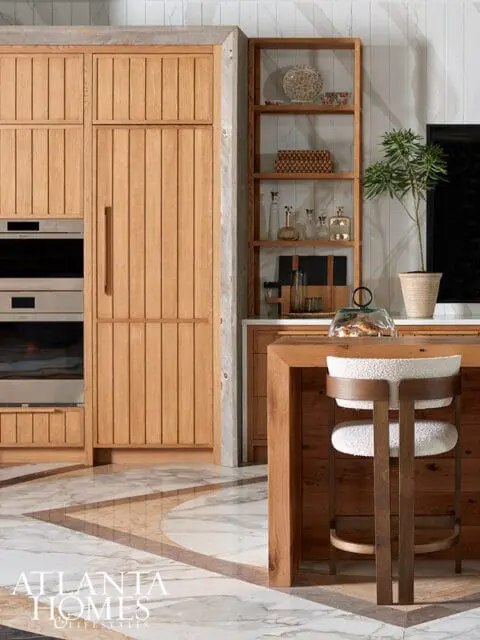 Wood-paneled kitchen with integrated appliances, open shelving, and a bar stool at a wood island.