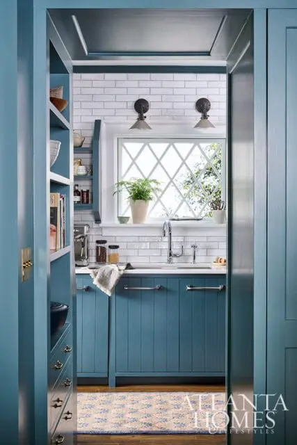 Blue kitchen with white subway tile backsplash, diamond-paned window, and stainless steel faucet.