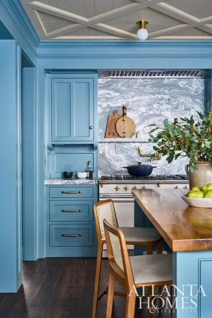 Blue kitchen cabinets with marble backsplash and wooden island with bar stools.