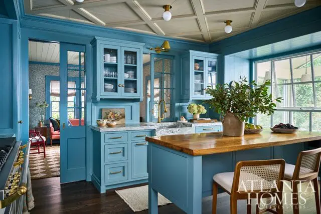 Blue kitchen with custom cabinetry, marble countertops, and a wooden island with cane-backed chairs.