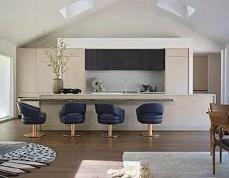 Modern kitchen with light wood cabinetry, dark upper cabinets, and navy swivel bar stools at a long